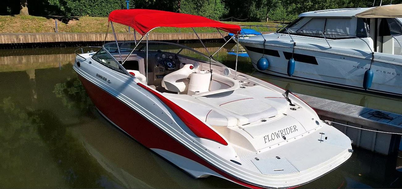 Rinker Captiva 246 mit rotem Bimini passend zu den roten Farbstreifen des Bootes von schräg hinten gesehen